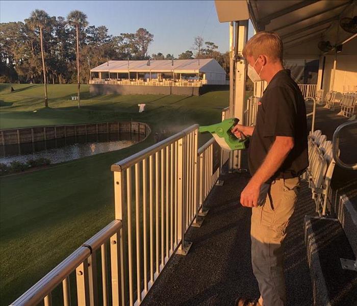 Image shows SERVPRO team member in black shirt and khaki pants applying electrostatic treatment to hand rails.