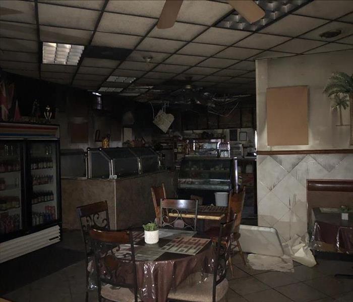 Photo shows part of a restaurant dining room with soot covering a table, a cooler, and a buffet line.