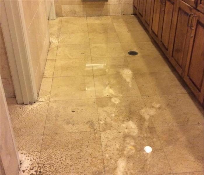 Photo shows dirty flood water on the tile floor in a women's restroom, between bathroom stalls and sink area.