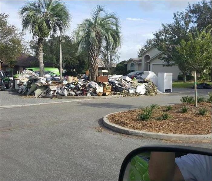 Image shows residential street, palm trees, and large piles of debris.