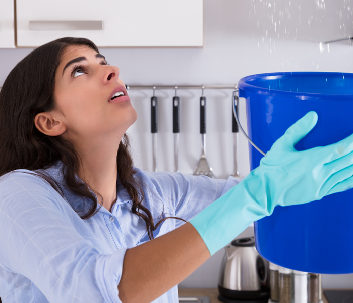 Women with gloves holding up a bucket to catch water from a leak.